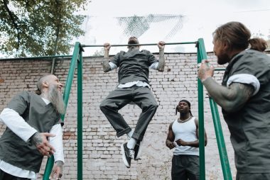 Men of diverse backgrounds exercising at an outdoor pull-up bar under trees.