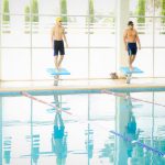 Athletes in swimwear on diving boards ready for a swim race in an indoor pool.